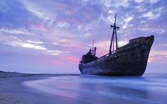 an old ship sitting on top of the ocean at sunset or dawn with clouds in the sky