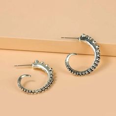 a pair of silver hoop earrings sitting on top of a beige surface with an orange background