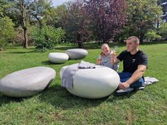 a man and woman sitting on the grass in front of large rock sculptures with drinks