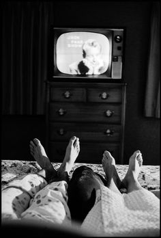 a person laying on a bed in front of a tv with their feet propped up