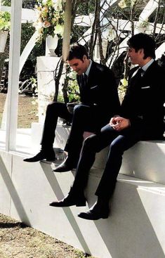 two men in suits sitting on a white bench