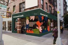 a woman walking down the sidewalk in front of a restaurant called chobani cafe