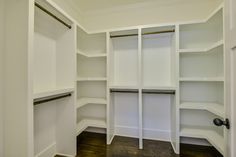 an empty walk in closet with white shelving and wood flooring on the side