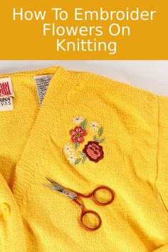 a pair of scissors sitting on top of a yellow sweater with flowers embroidered on it