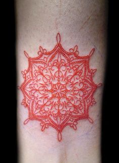 a red ink tattoo on the back of a person's arm with an intricate design