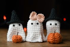 three crocheted white ghost dolls with black hats and orange pumpkins on a wooden table