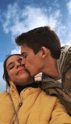 a young man and woman are kissing each other in front of a blue sky with white clouds