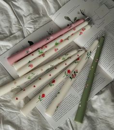 six white candles with flowers on them are next to an open book and a pen