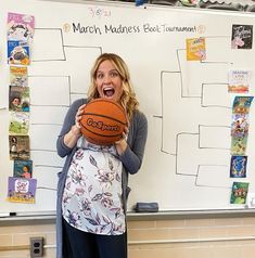 a woman standing in front of a whiteboard holding a basketball and making a funny face