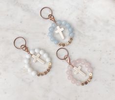 three keychains with cross charms on them sitting on a marble countertop next to each other