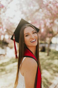 a woman wearing a graduation cap and gown in front of some trees with pink flowers