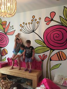 two children are standing on a pink bench in front of a flowered wall mural