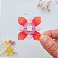 someone is holding up an origami piece with flowers in the backgroun