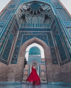 a woman in a red dress is standing under an archway at the top of a building