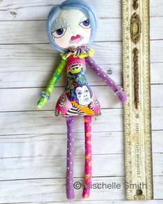 a colorful doll is next to a ruler on a white wooden wall with planks