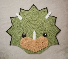 a green crocheted hedge rug with black eyes and brown nose is on the floor