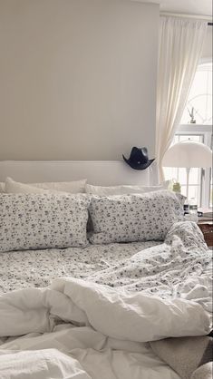 an unmade bed with white sheets and blue flowers on the comforter is in front of a window