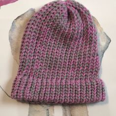 a pink and gray knitted hat sitting on top of a piece of paper next to scissors