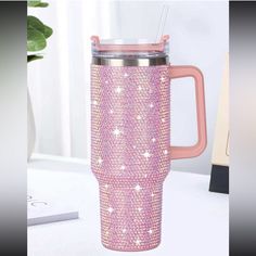 a pink and silver cup sitting on top of a white table next to a plant