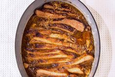 a pan filled with meat and sauce on top of a white table cloth next to a knife