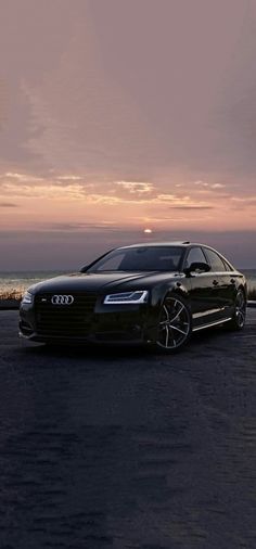 a black car parked in front of the ocean at sunset or dawn with its lights on