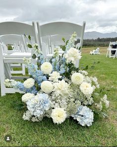 a bouquet of flowers sitting on top of a grass covered field next to two white chairs