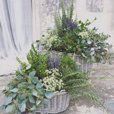 three wicker baskets filled with flowers and greenery sitting on the side of a building