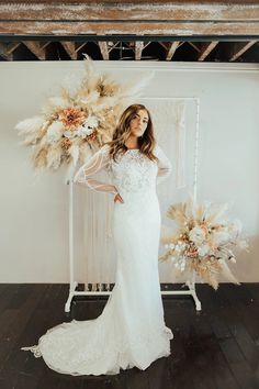 a woman standing in front of a white backdrop with flowers and feathers on the wall