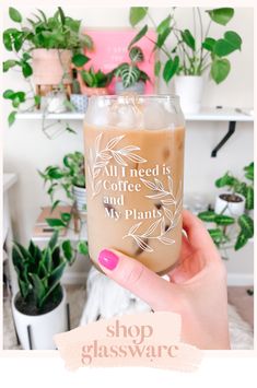 a person holding up a glass with coffee and plants in it