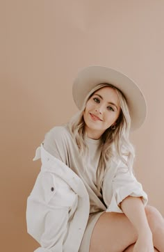 a woman sitting on the ground wearing a hat and white shirt with her legs crossed