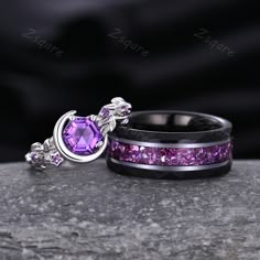 two rings with purple stones on them sitting on top of a gray rock next to each other