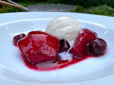 a white plate topped with ice cream and cherries on top of red jelly sauce