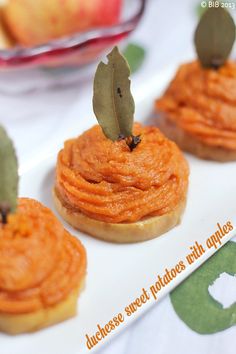 three small pastries with leaves on them sitting on a white plate next to an apple