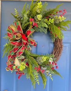 a christmas wreath on a blue door with greenery and red berries hanging from it