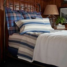 a bed with blue and white striped sheets in a wooden cabin style bedroom, next to a lamp