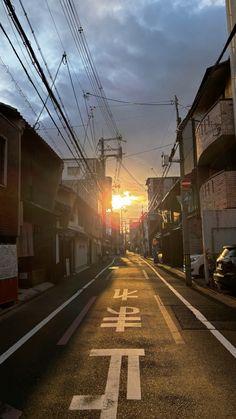 the sun is setting on an empty street with power lines in the sky above it