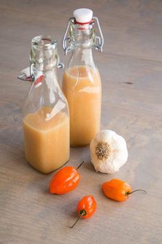 two glass bottles filled with liquid next to peppers and garlic on a wooden counter top