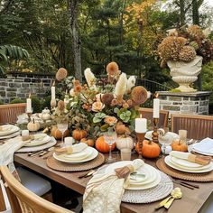 an outdoor table set for thanksgiving dinner with pumpkins and greenery in the background