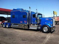 a blue semi truck parked in front of a gas station