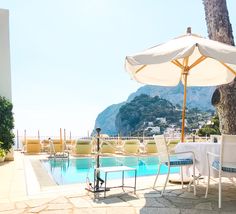 an outdoor pool with chairs and umbrellas next to the water in front of mountains