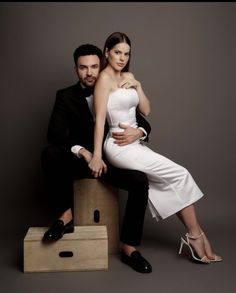 a man and woman sitting on top of a wooden box posing for the camera with their arms around each other