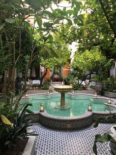 a fountain in the middle of a courtyard surrounded by greenery and potted trees