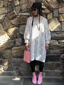 a woman standing in front of a stone wall holding a pink purse and wearing a black hat