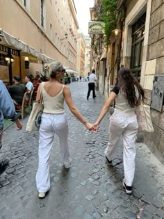 two women are holding hands while walking down the street in front of some people and buildings