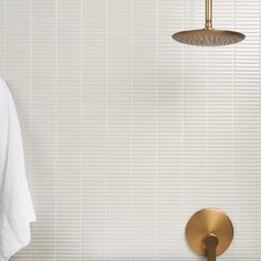 a bathroom with white tile and gold faucet, shower head and hand held showerhead