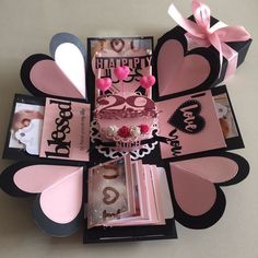 a pink and black heart shaped box with cards, pictures, and other items in it