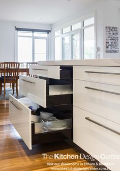 an open drawer in the middle of a kitchen with wooden flooring and white cabinets