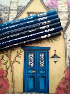 six colored pencils sitting in front of a drawing of a blue door and tree