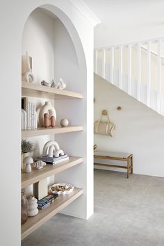 a white room with shelves filled with vases and other items on the wall next to a staircase