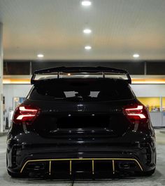 the rear end of a black car parked in a garage with its hood up and lights on